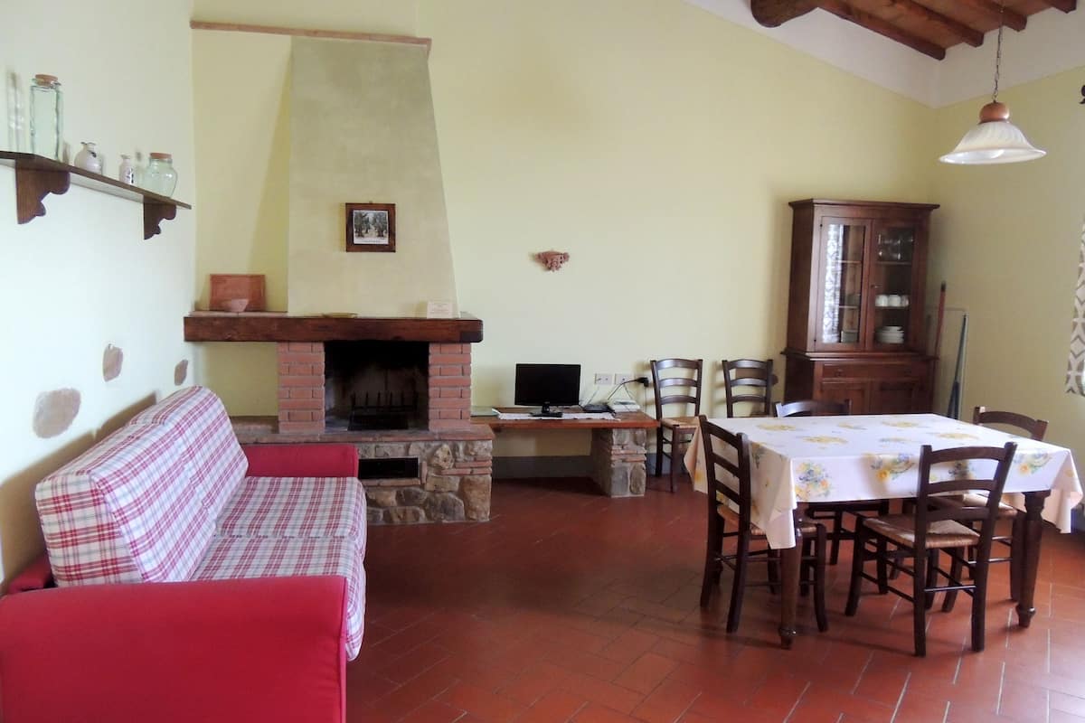 Una sala de estar acogedora con chimenea, una mesa de comedor con sillas, un sofá rojo y un aparador de madera.