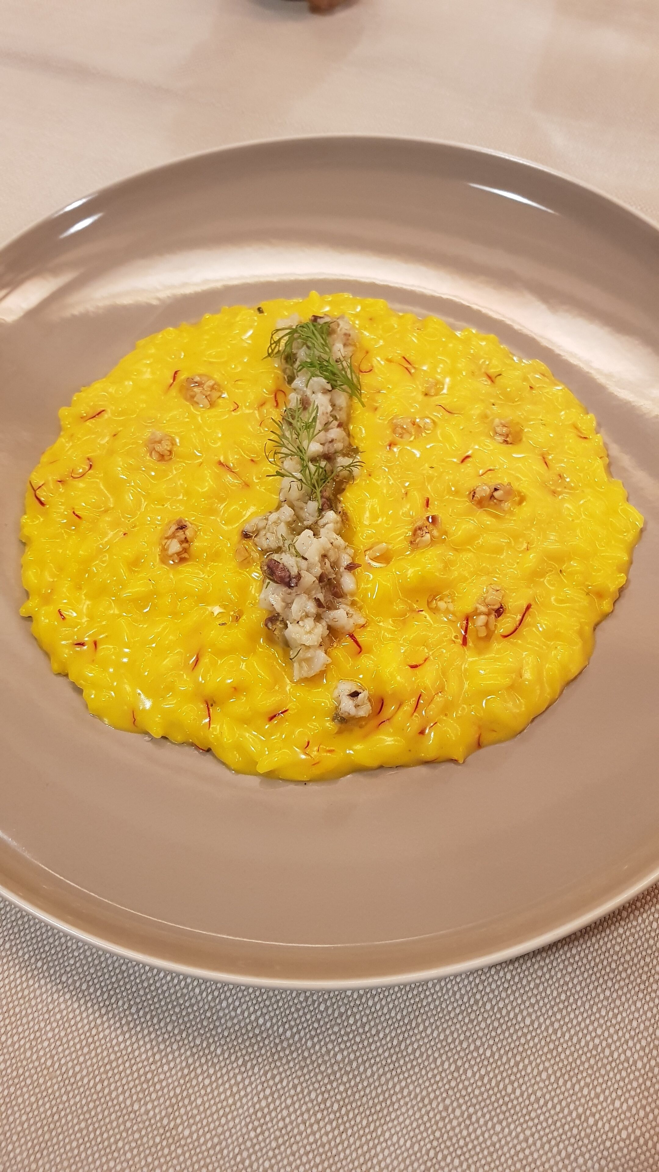 Une assiette de nourriture jaune, garnie de noix et d’herbes.