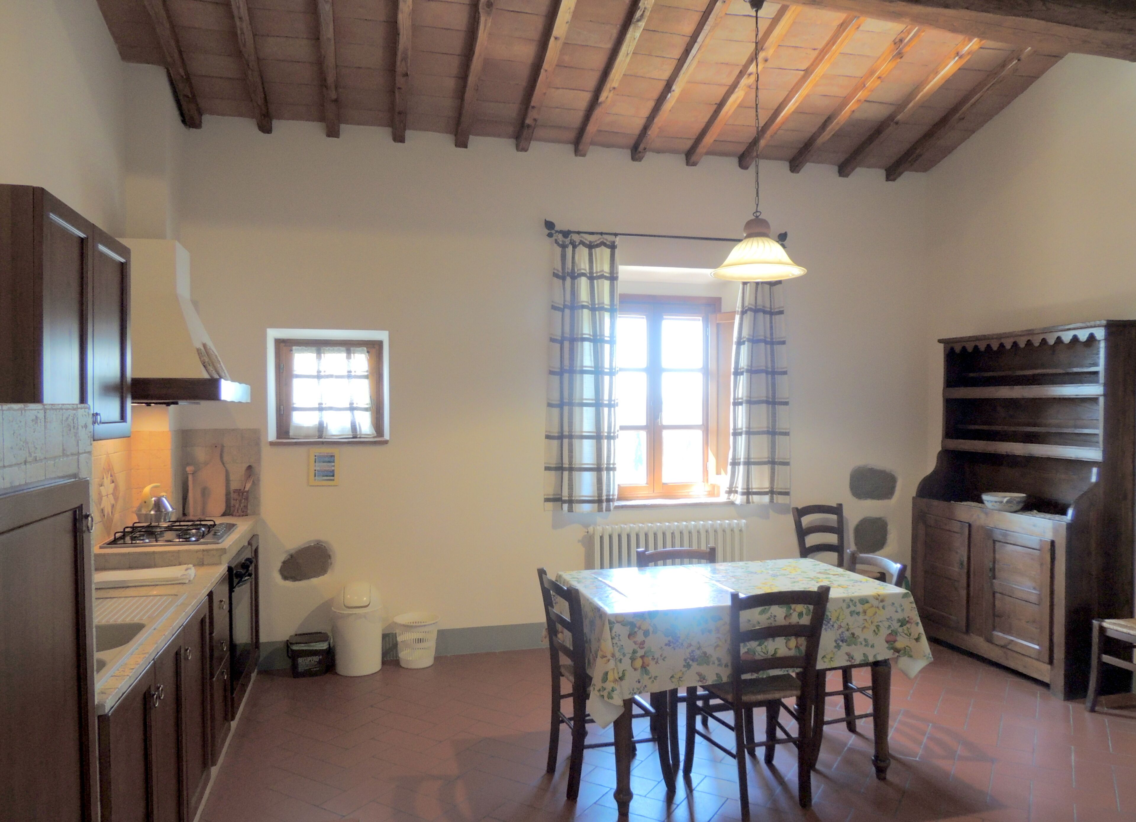Uma cozinha rústica com vigas de madeira, fogão a gás, mesa de jantar com cadeiras e janela com cortinas.