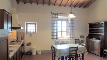 Uma cozinha rústica com vigas de madeira, fogão a gás, mesa de jantar com cadeiras e janela com cortinas.