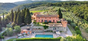 A large villa with a swimming pool, surrounded by lush greenery and hills.