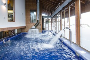 A hot tub with multiple water jets, wooden beams, and a view of the outside through large windows.