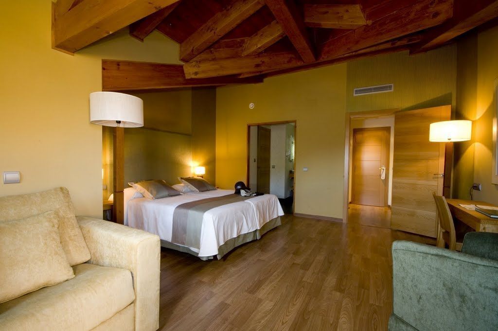Habitación de hotel con cama, sofá, mesa de comedor y techo de madera.