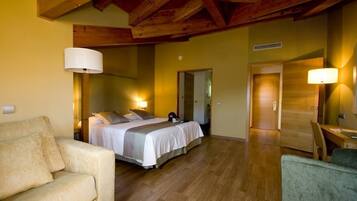 Habitación de hotel con cama, sofá, mesa de comedor y techo de madera.