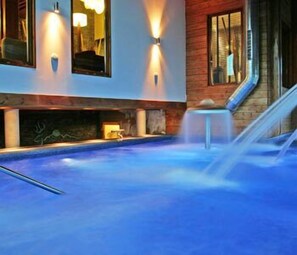 A modern indoor pool area with a blue floor, a small waterfall feature, and wall-mounted lighting. - Arha Reserva del Saja (Valle de Cabuerniga)