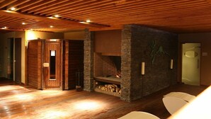 A room with a wooden ceiling, a stone fireplace, and a door leading to another area.