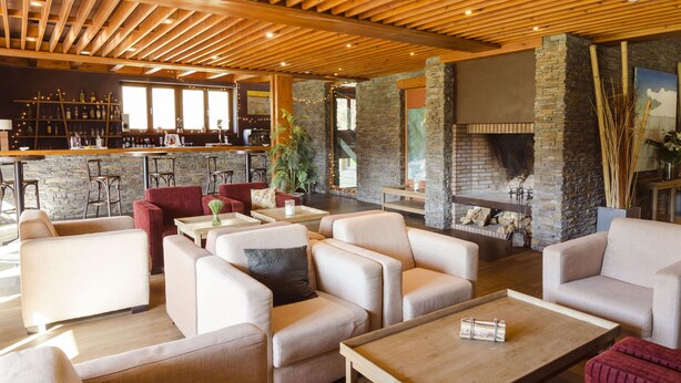Un área de lounge moderna con sofás, una mesa de centro y una barra con pared de piedra y techo de madera.