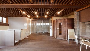 A spacious hallway with wooden flooring, a stone fireplace, and a seating area with white chairs.