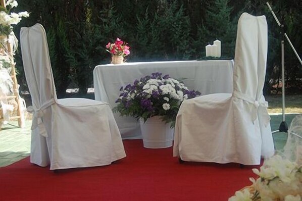 Two white chairs with white covers, a table with a white tablecloth, and a bouquet of flowers.