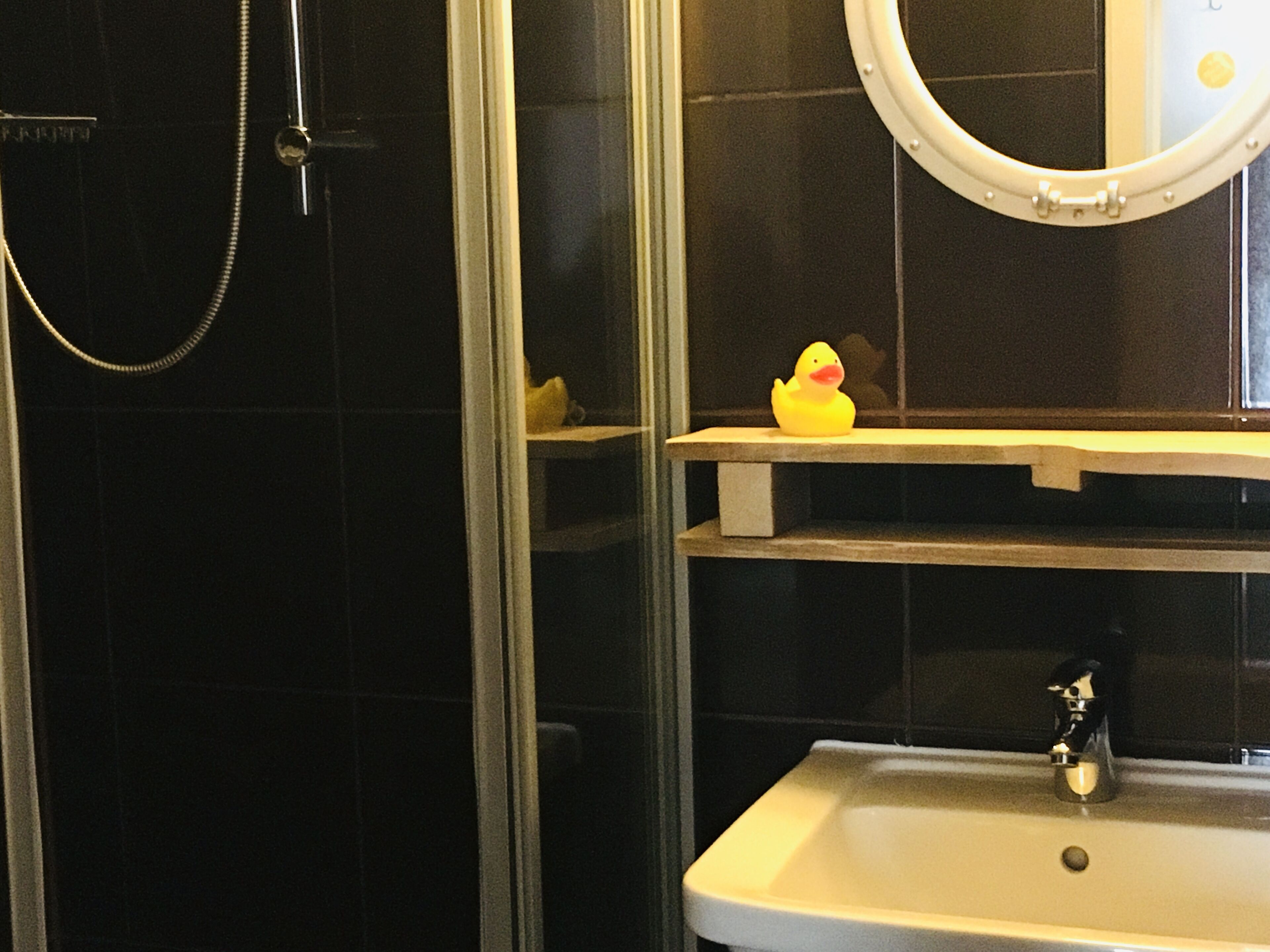 Un bagno con doccia vetrata, lavandino bianco, specchio e ripiano con un'anatra di gomma.