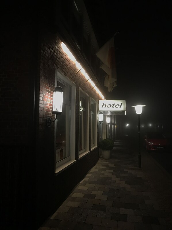 Exterior de un hotel de noche con señalización iluminada, fachada de ladrillo y un paseo empedrado.
