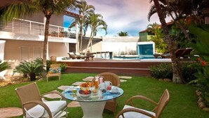 A patio with wicker chairs and a glass table set for breakfast, overlooking a swimming pool and a two-story building. - Armacao dos Buzios Pousada Design (Búzios)