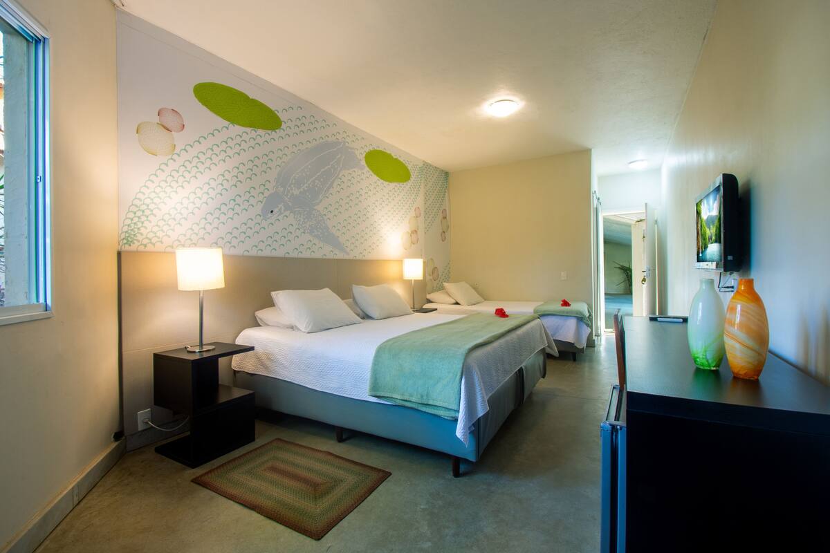 A modern hotel room with a large bed, bedside lamps, a flat-screen TV, and a decorative wall mural.