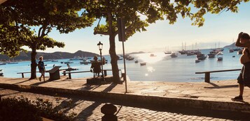 Um calçadão à beira-mar com bancos de pedra, um poste de luz e uma estátua.
