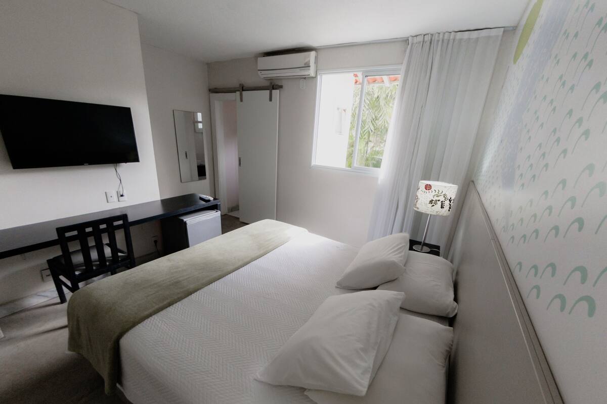A hotel room with a bed, a desk, a chair, a TV, and a window with curtains.