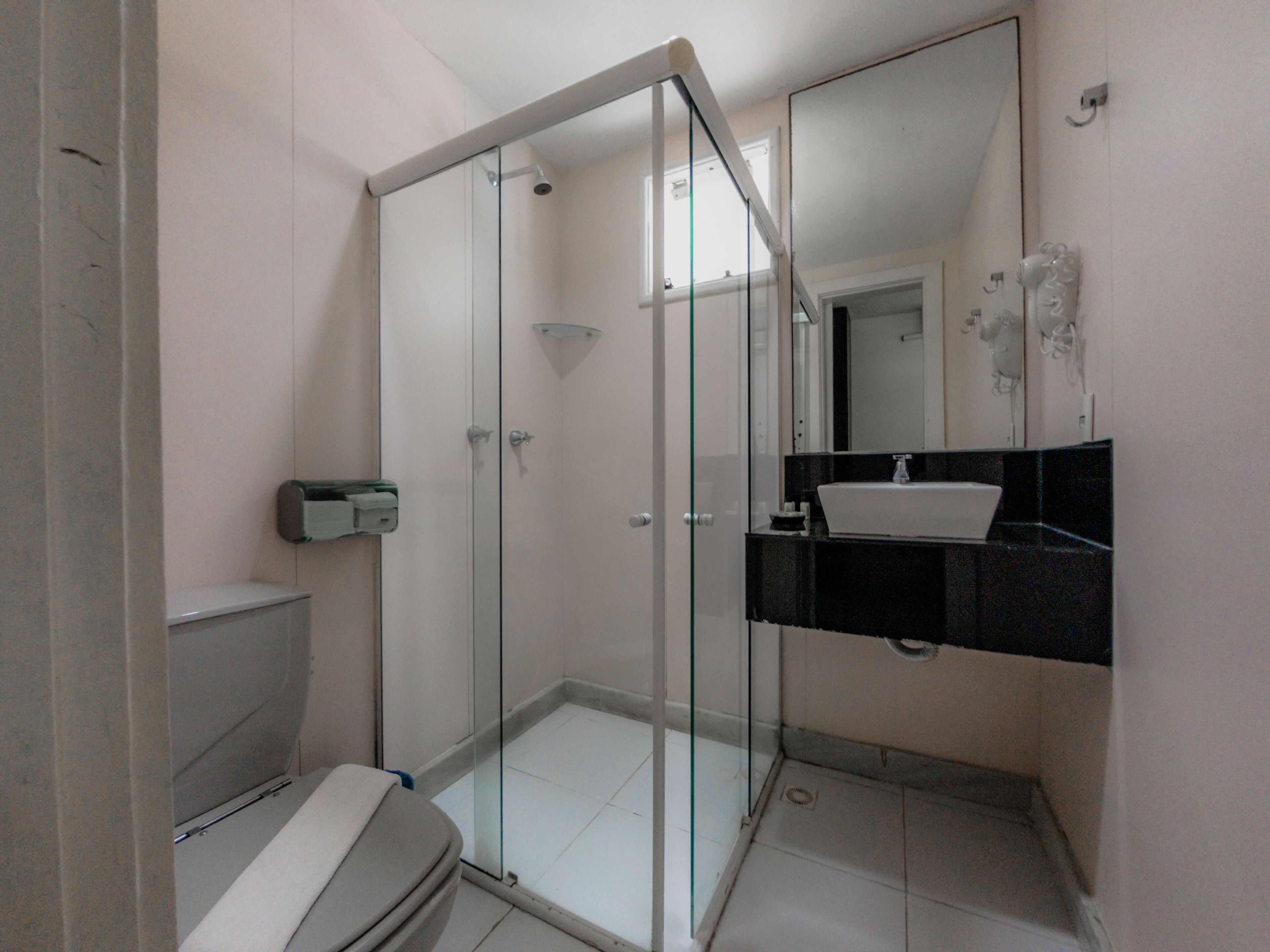 Un baño con cabina de ducha de vidrio, inodoro y lavamanos con encimera negra.