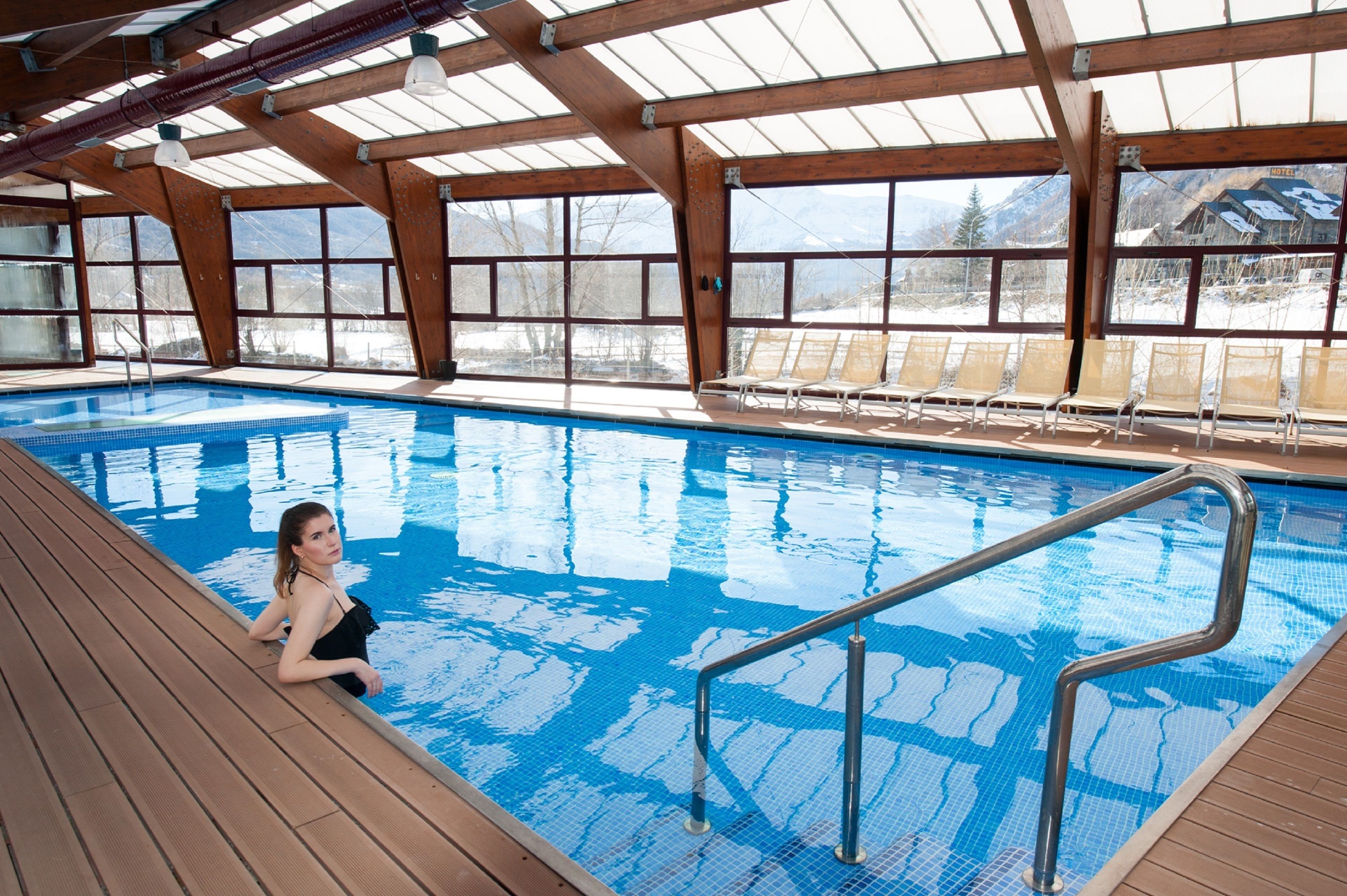 An indoor swimming pool with clear blue water, wooden deck, and lounge chairs.