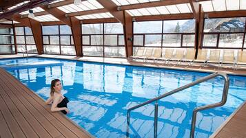 An indoor swimming pool with clear blue water, wooden deck, and lounge chairs.