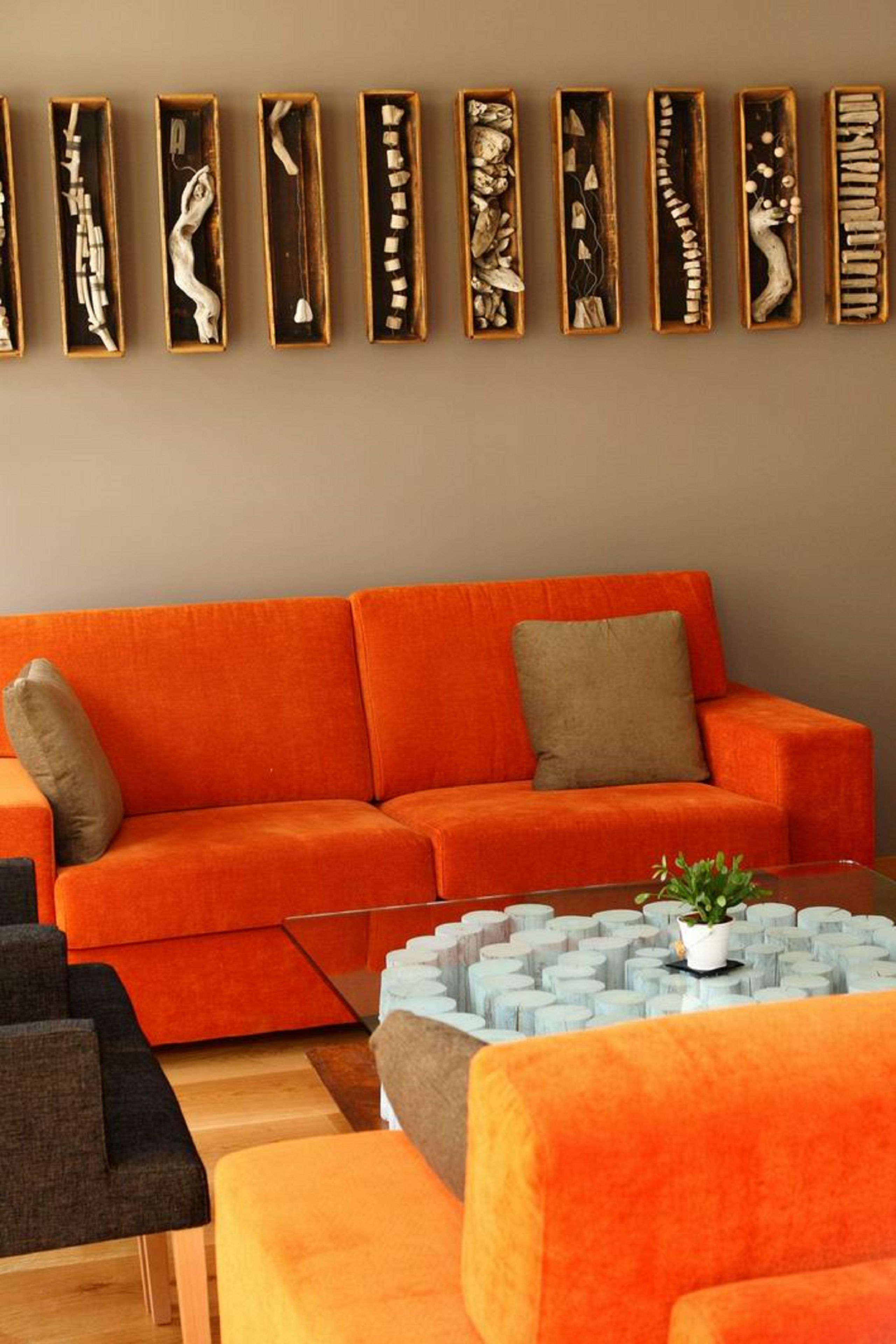 Una sala de estar moderna con un sofá naranja, una mesa de centro de vidrio y una exposición de arte en la pared.