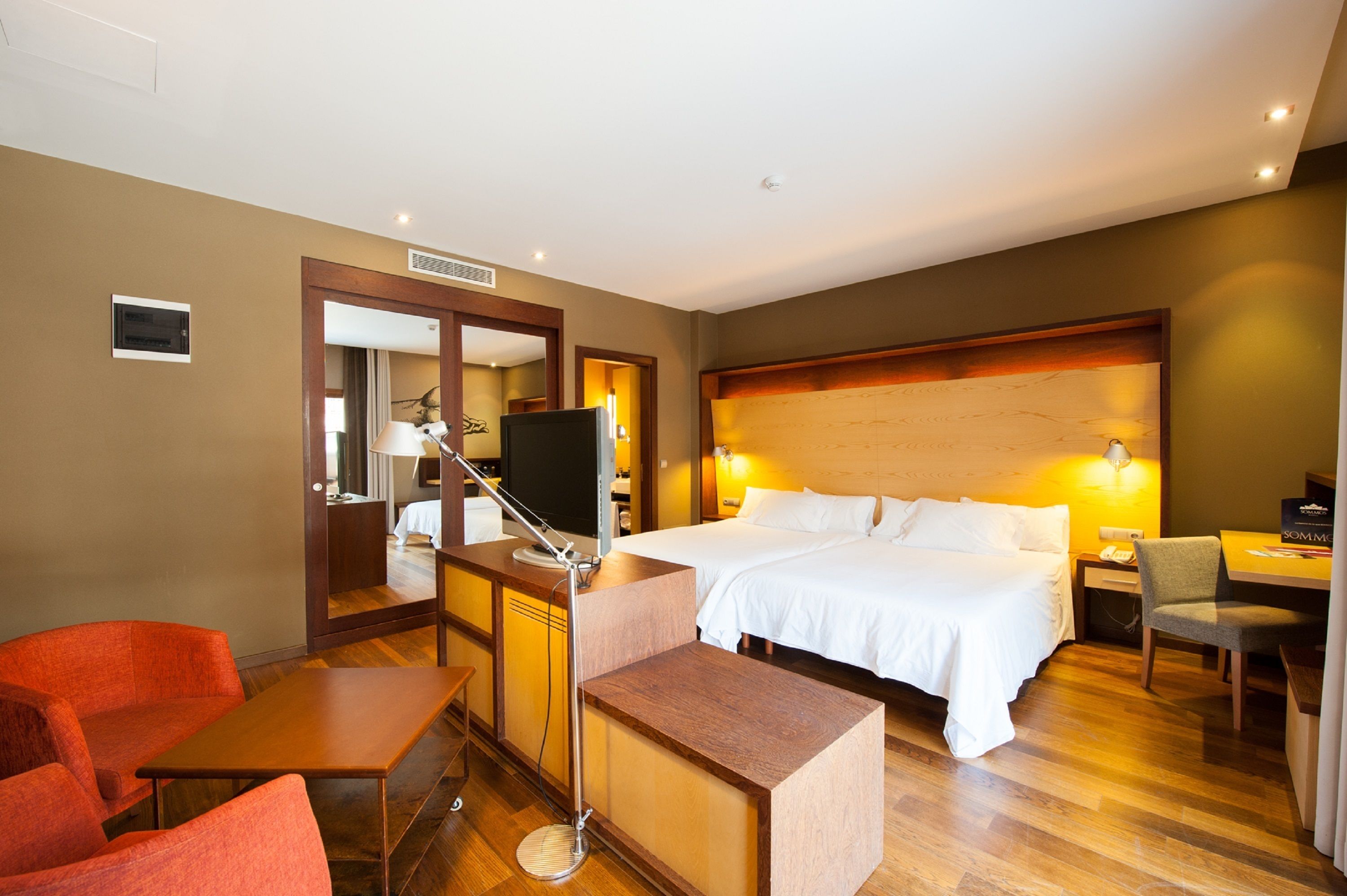 Ein Hotelzimmer mit Bett, Schreibtisch, Stuhl, Fernseher und Spiegel.