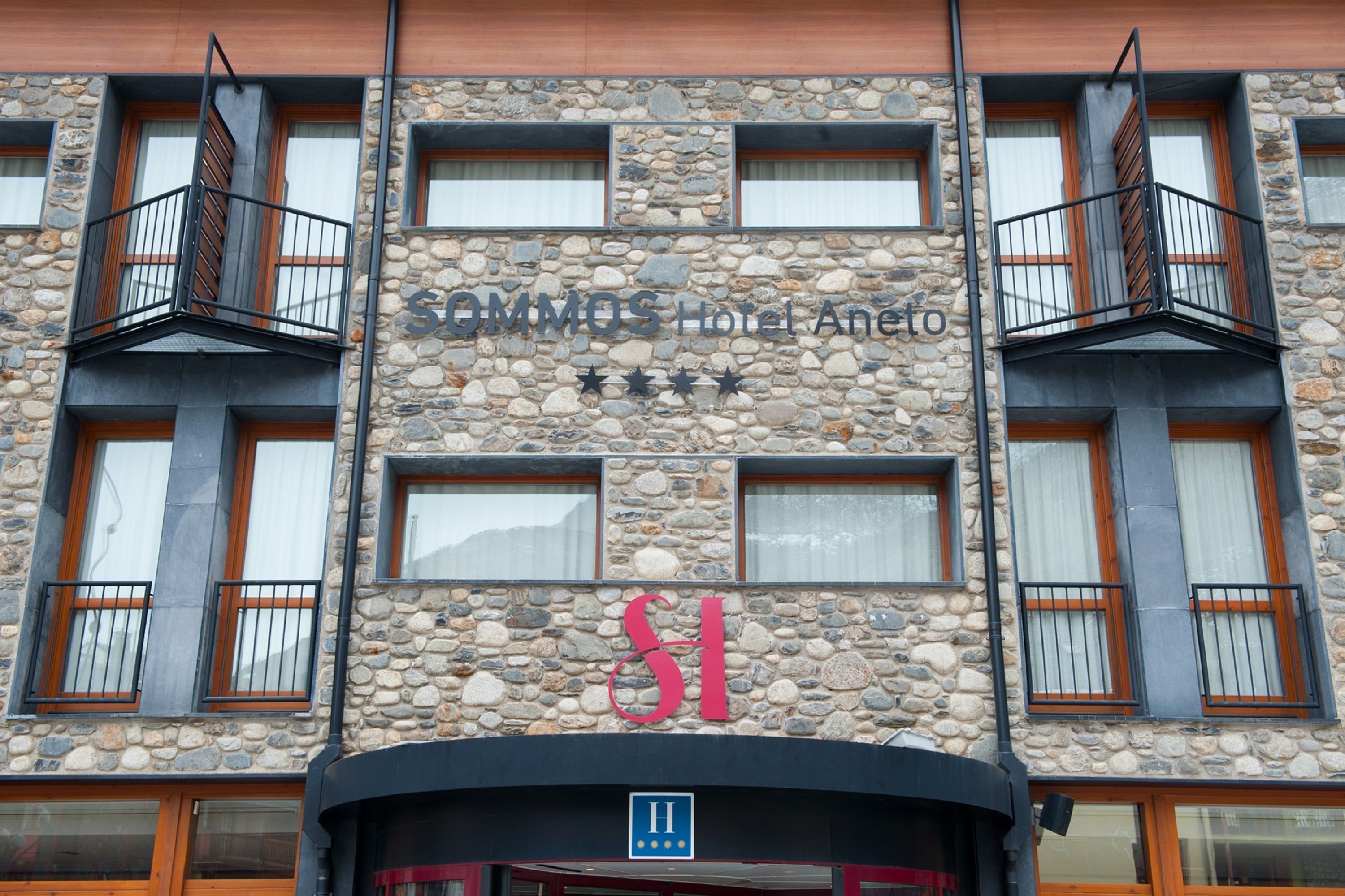 A hotel facade with a stone exterior, balconies with metal railings, and a sign indicating it is a hotel.