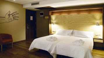 A hotel room with a large bed, two bedside tables with lamps, a wooden headboard, a red chair, and a wall art piece.
