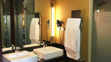 A hotel bathroom with two sinks, a large mirror, and a hairdryer.