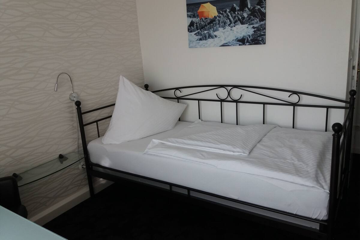 A bed with a metal frame, white bedding, and a single pillow.