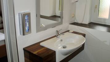 A bathroom with a white sink, a wooden vanity, a mirror, a hairdryer, and a soap dispenser.