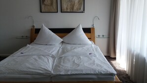 Cama bem arrumada com lençóis brancos e duas almofadas, cabeceira de madeira e duas obras de arte emolduradas na parede.
