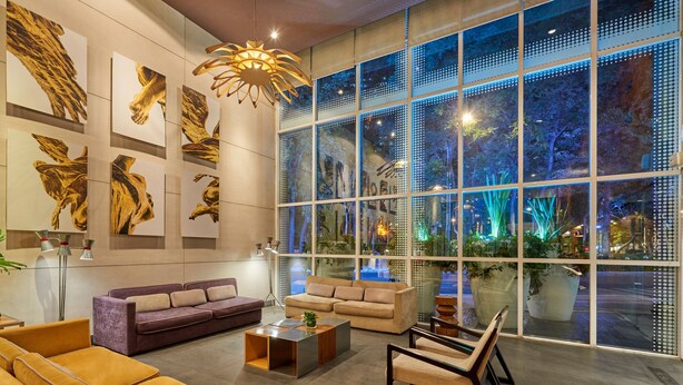 A modern interior with a large window, a sofa, a coffee table, and abstract wall art. - City Express Plus by Marriott Ciudad de México Reforma El Ángel (Mexico City)