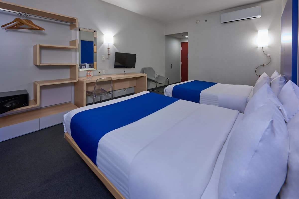 Habitación de hotel con dos camas, un escritorio, un televisor y un espejo.