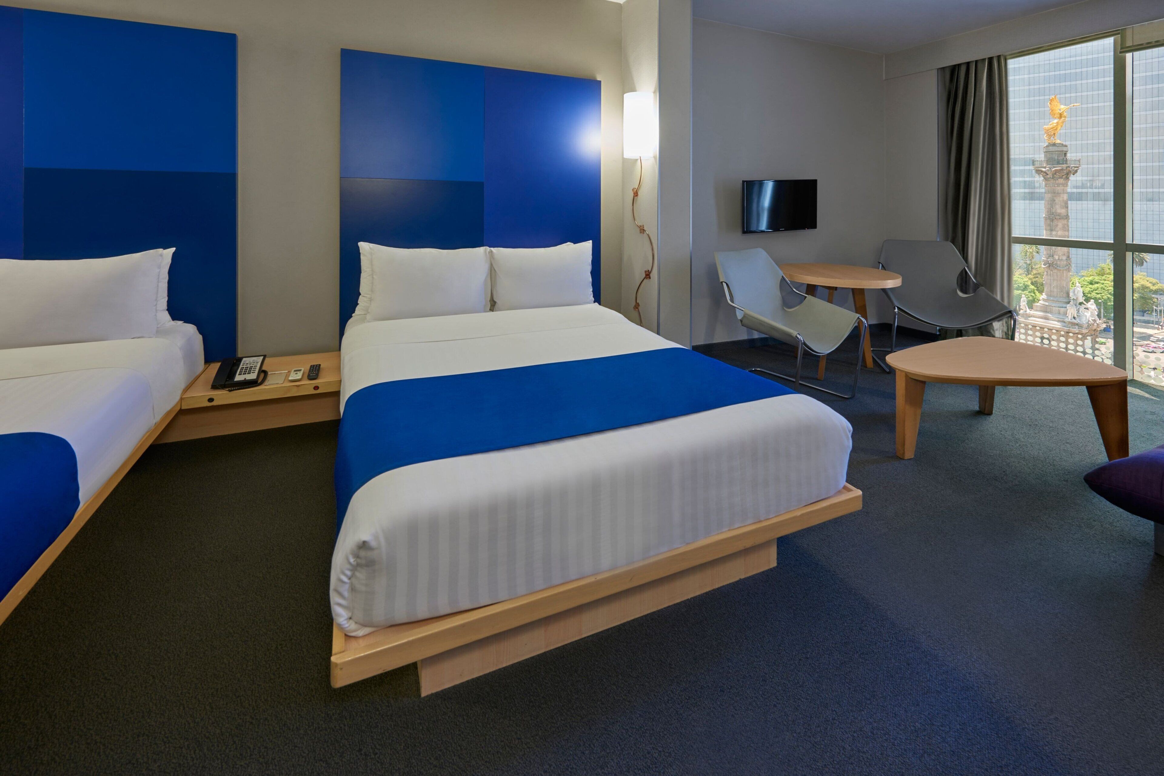 A hotel room with a large bed, two bedside tables, a desk, a chair, and a TV.