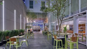 An indoor courtyard with green chairs and tables, surrounded by glass walls and plants. - City Express Plus by Marriott Ciudad de México Reforma El Ángel (Mexico City)