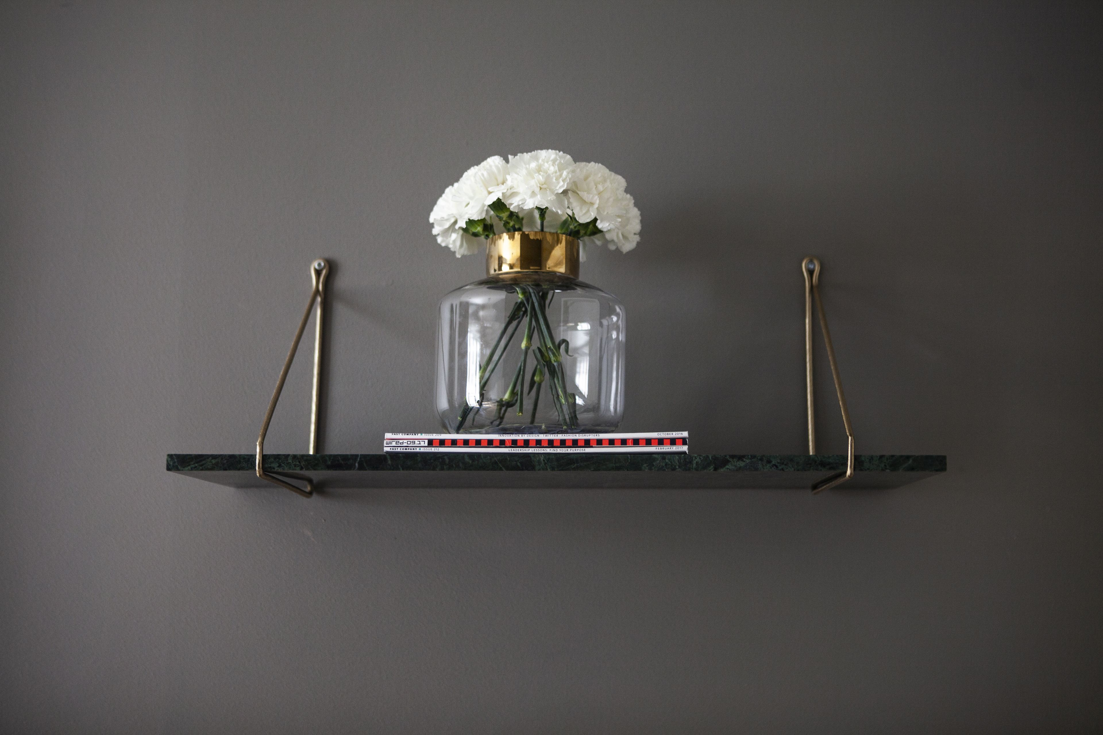 A clear glass vase with white flowers on a marble shelf against a grey wall.