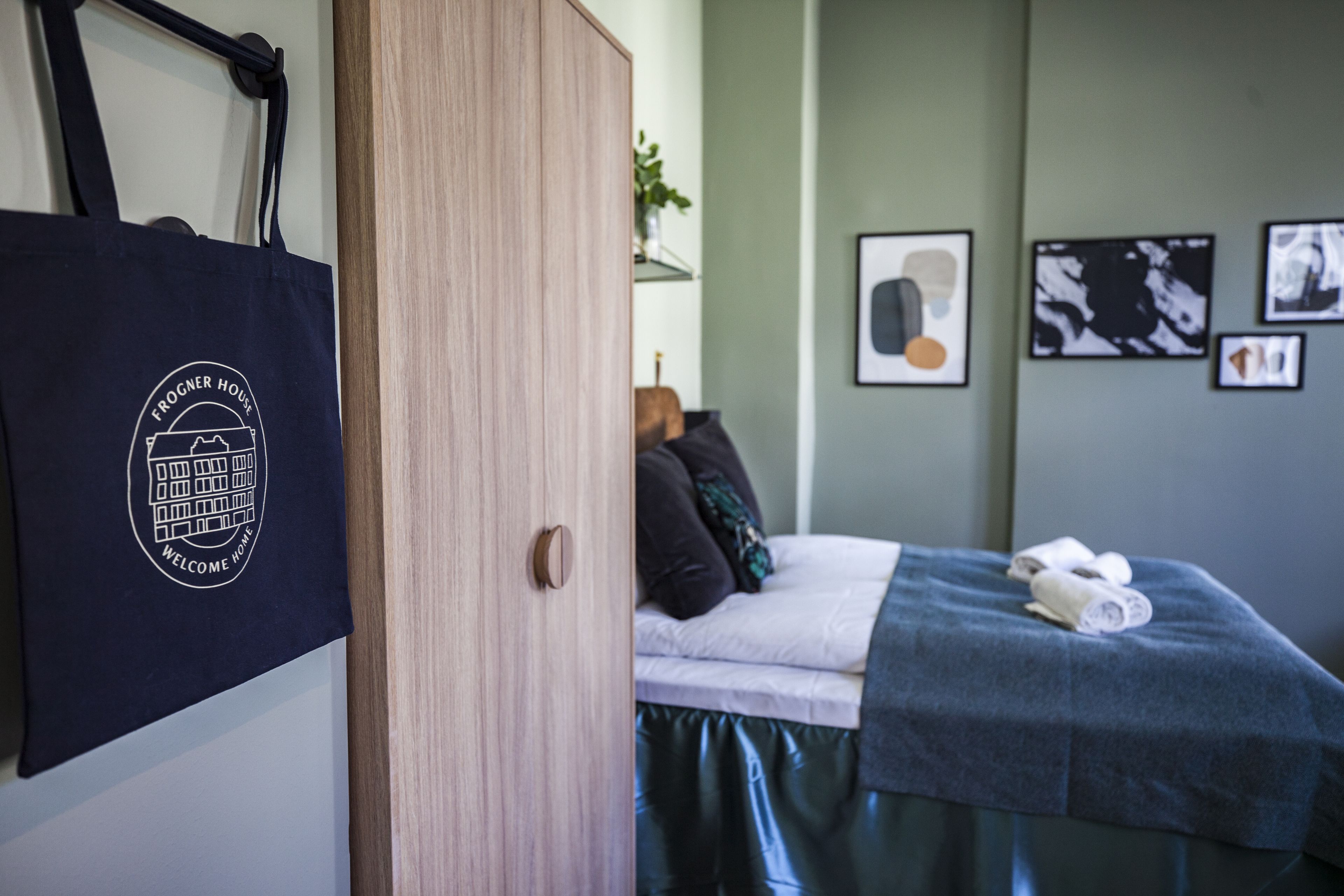 Ett hotellrum med en säng, en garderob i trä, en handduk och en välkomstpåse.