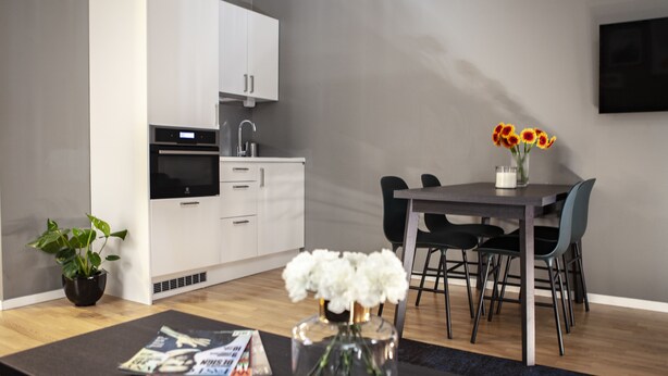 Une cuisine moderne avec des meubles blancs, une table à manger avec des chaises et un vase de fleurs posé sur la table.