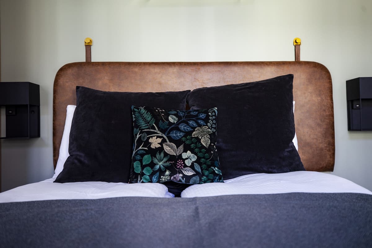 Een bed met een houten hoofdbord, twee zwarte kussens en een kussen met een bloemmotief.