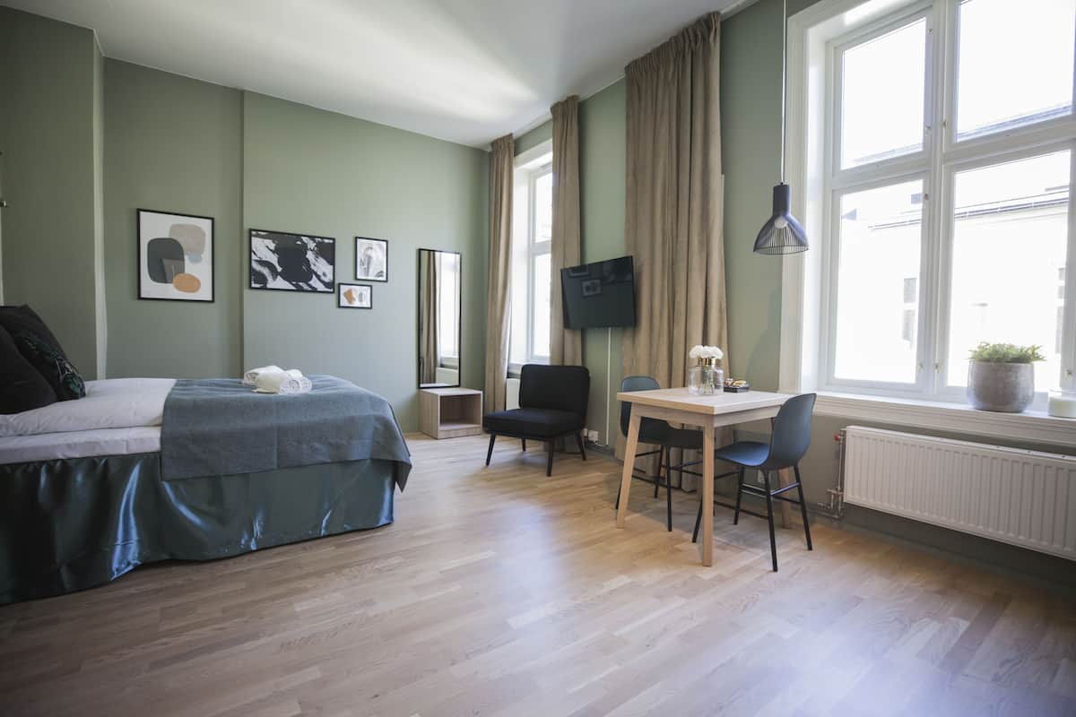 Een slaapkamer met een bed, een bureau en een stoel. Er is een televisie aan de muur en een raam met gordijnen.