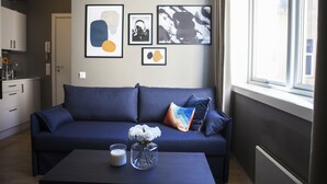 Un salon moderne avec un canapé bleu foncé, une table basse ornée d’un vase de fleurs et des œuvres d’art accrochées au mur.