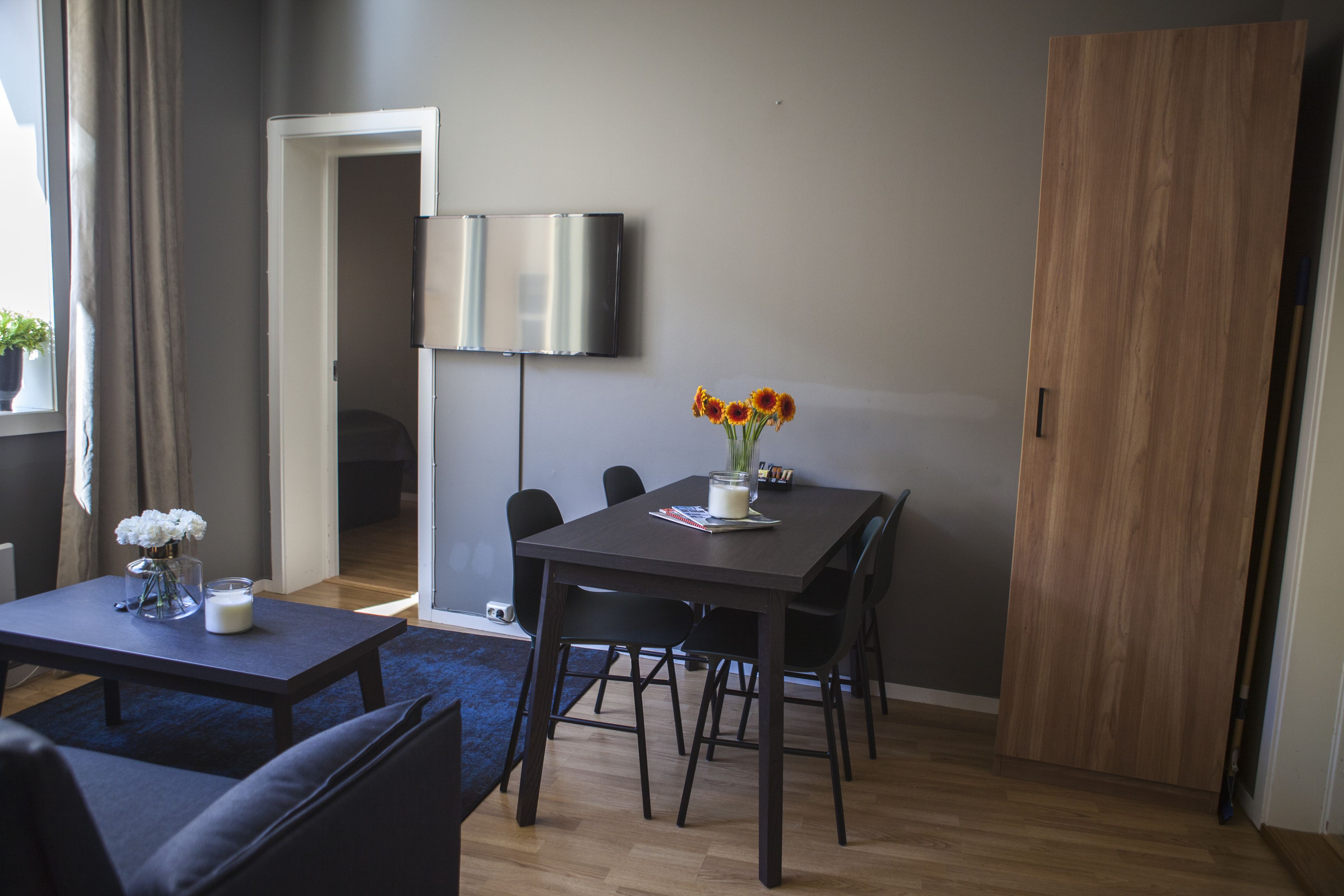 A modern living room with a dark wooden dining table, black chairs, a blue sofa, and a coffee table with a vase of flowers.