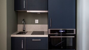 Une cuisine de taille réduite, dotée de meubles de rangement sombres, d’un évier et d’un four encastré.