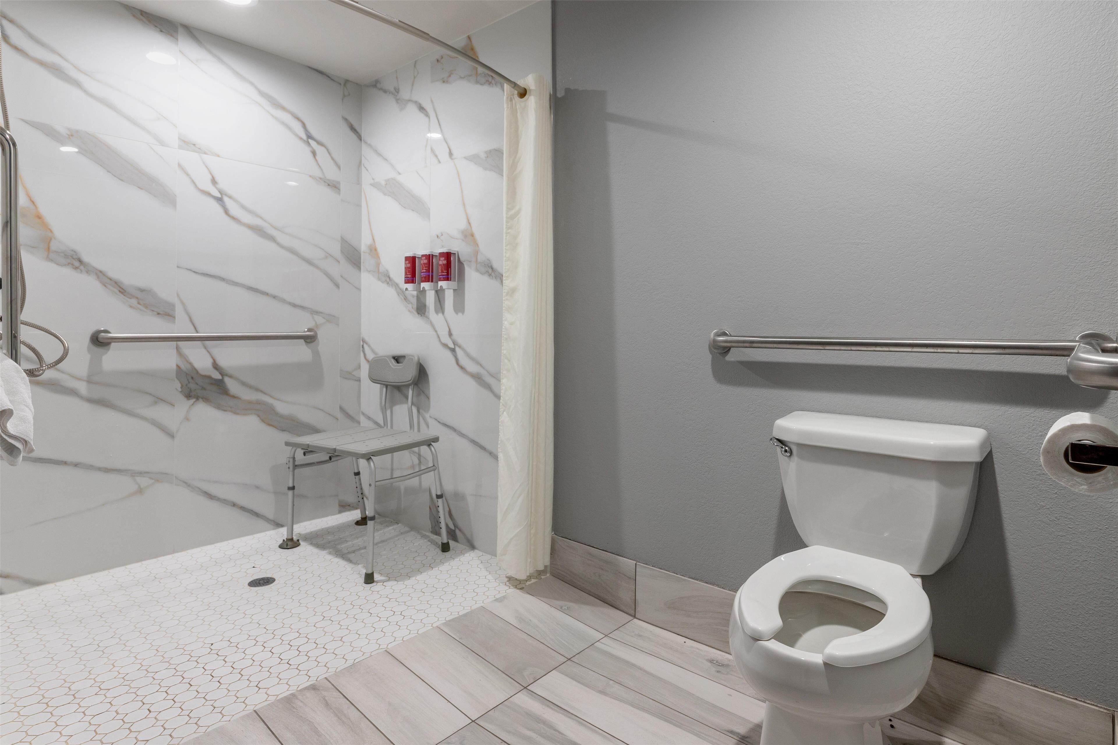 A modern bathroom with a marble shower wall, a grab bar, a toilet, and a small step stool.