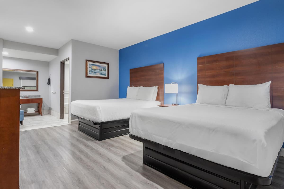 A hotel room with two beds, a wooden headboard, a small desk, and a painting on the wall.