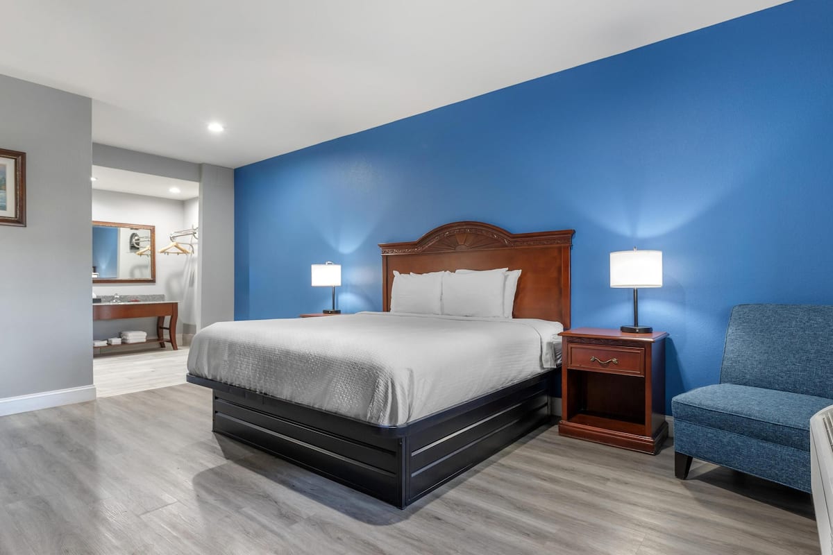 A bedroom with a large bed, two bedside tables with lamps, a chair, and a desk with a mirror.