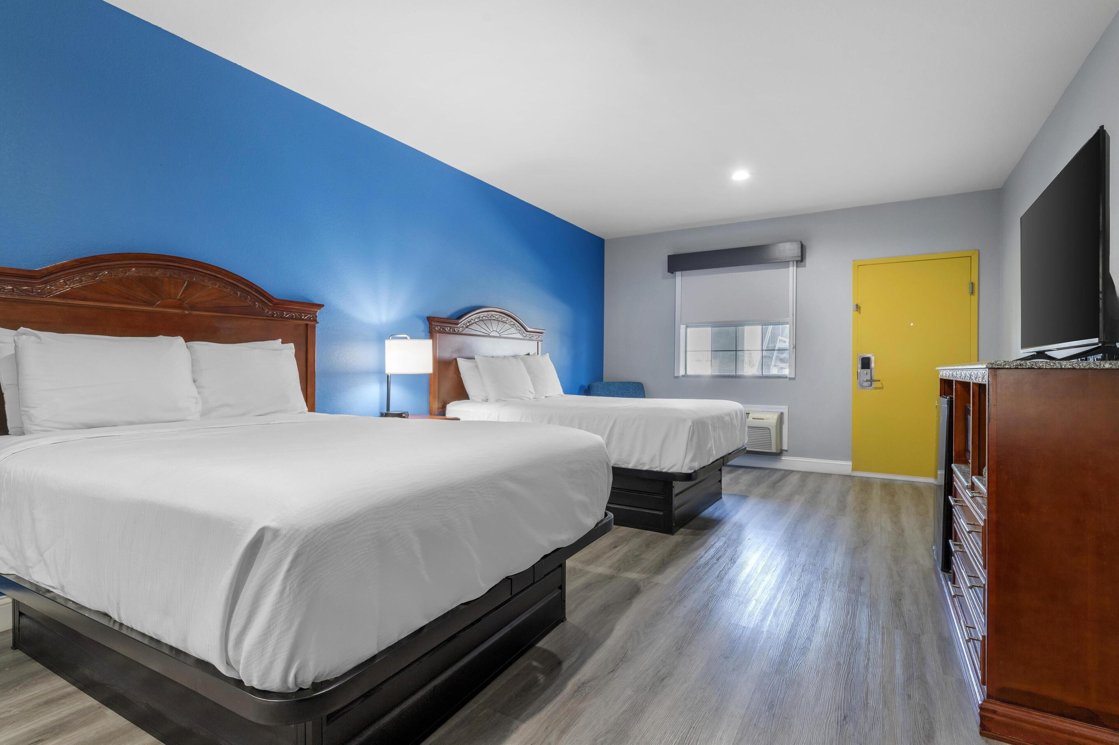 Habitación de hotel con dos camas, televisión, escritorio y una puerta amarilla.