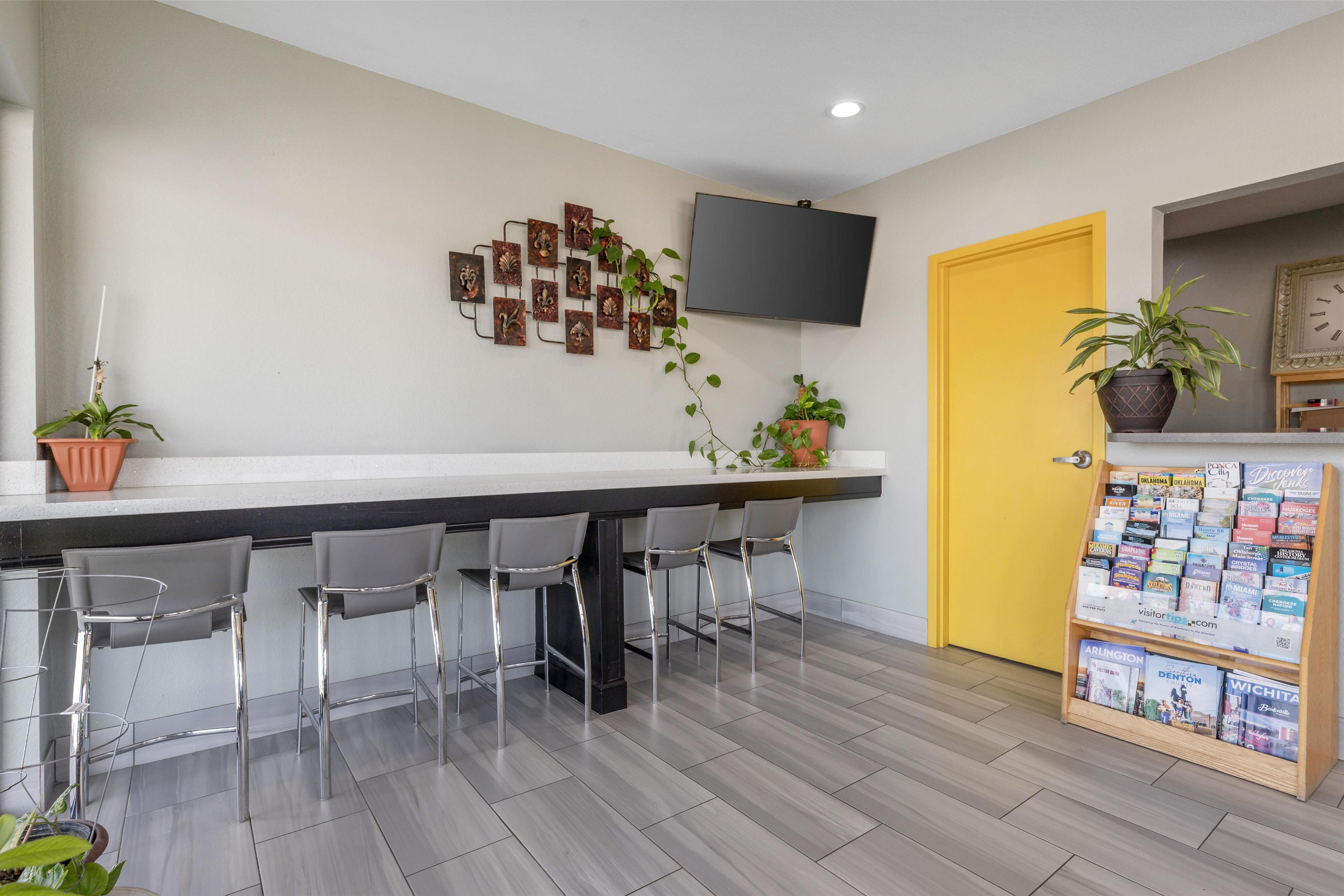 A modern bar area with a flat-screen TV, a yellow door, and a magazine rack.