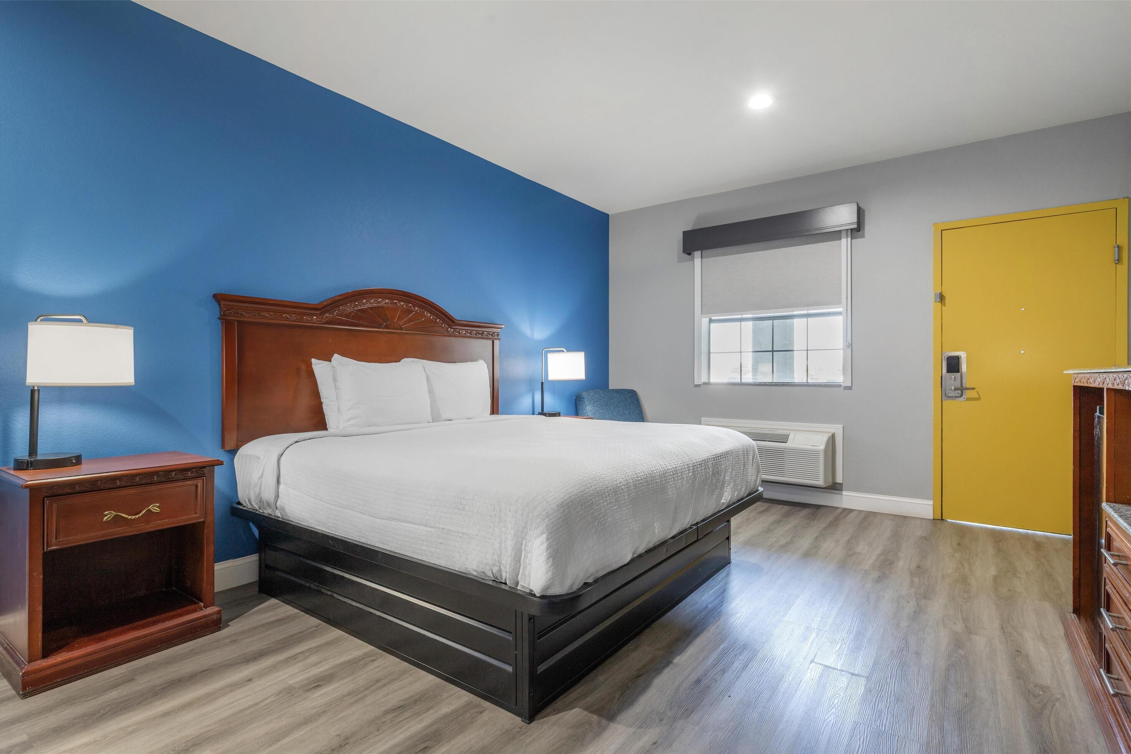 A hotel room with a wooden bed, a nightstand, a lamp, a window, and a door.