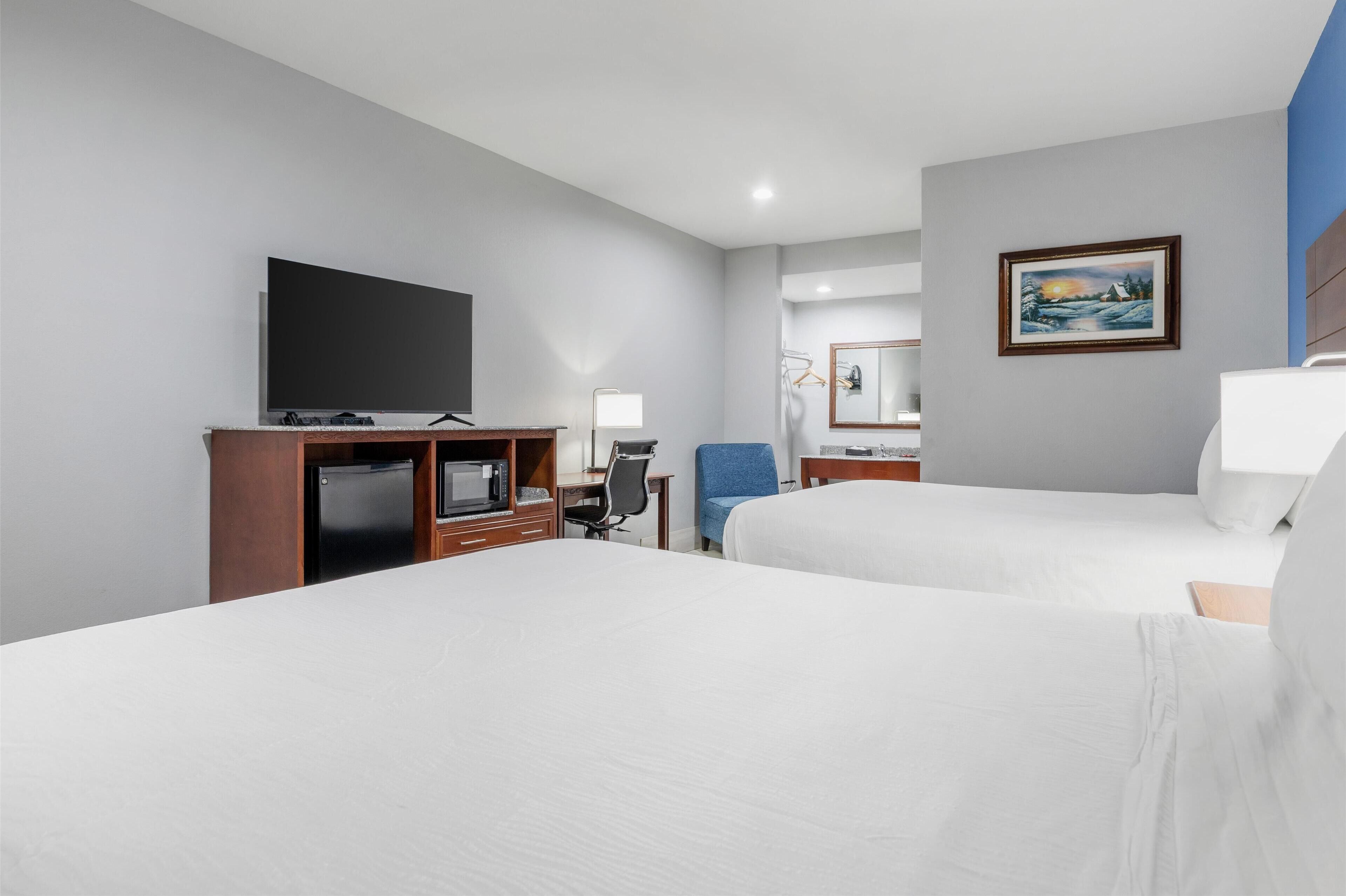 Habitación de hotel con dos camas, televisión, escritorio con silla, microondas y un cuadro en la pared.