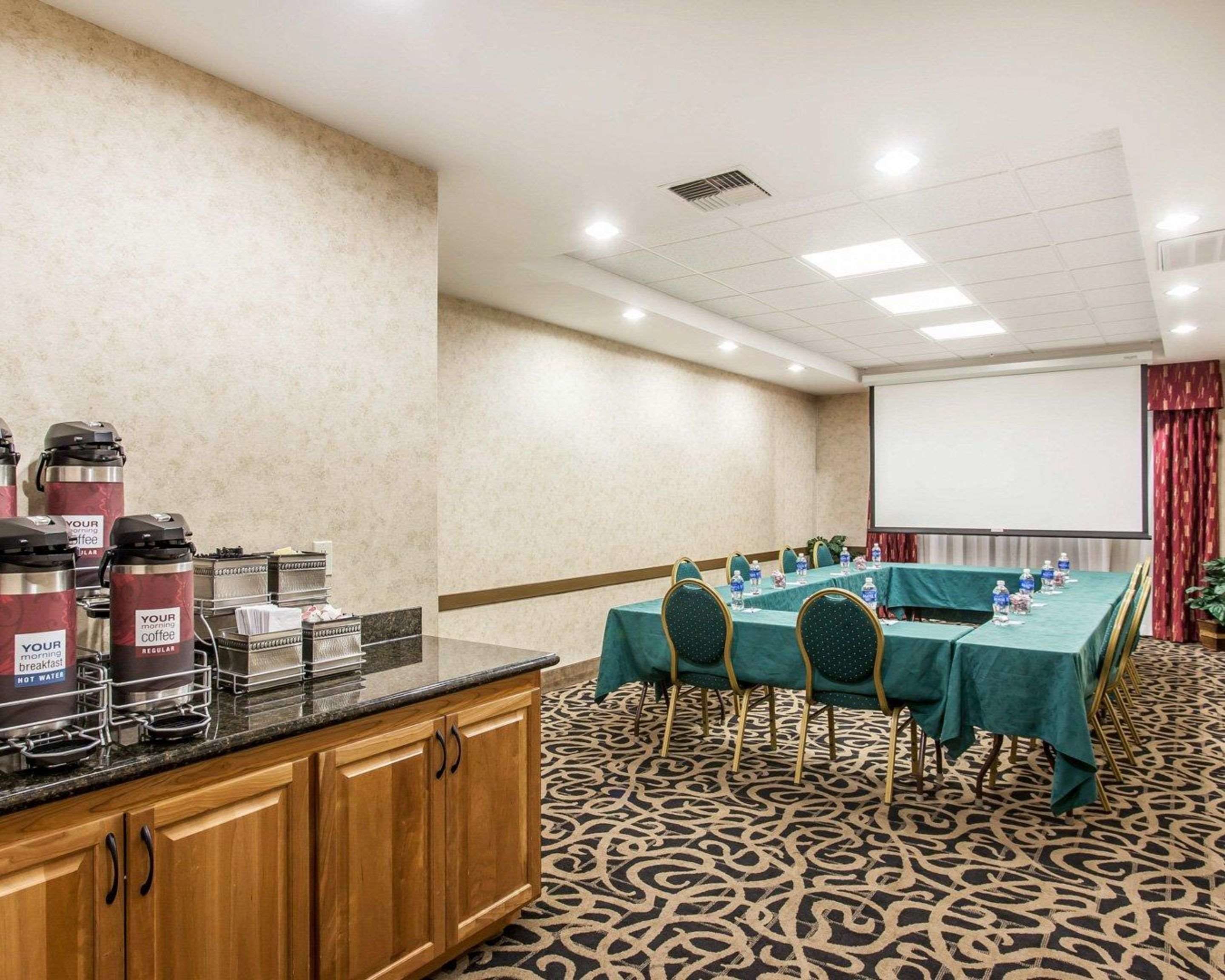 A conference room with a long table, chairs, a projector screen, and coffee dispensers.